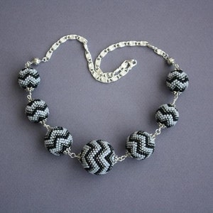 May include: A silver chain necklace with black and gray beaded balls. Each ball has a chevron pattern.