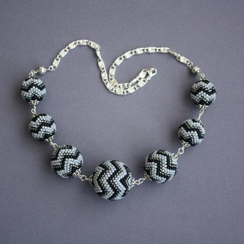 May include: A silver chain necklace with black and gray beaded balls. Each ball has a chevron pattern.