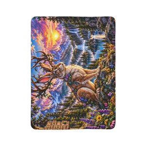 May include: A rectangular throw blanket featuring a jackalope with large antlers, surrounded by colourful wildflowers and pine trees. The background displays a vibrant sunset over mountains and a lake. A wooden sign reads WILD MYTHICAL FREE ALWAYS LONG.