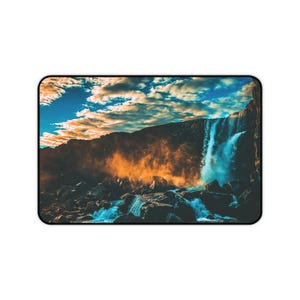 Peut inclure: Tapis de souris rectangulaire avec un paysage de cascade. L'image présente une cascade dévalant une falaise rocheuse, avec de l'eau bleue vibrante et un ciel dramatique avec des nuages. La scène est éclairée par la lumière dorée du soleil.