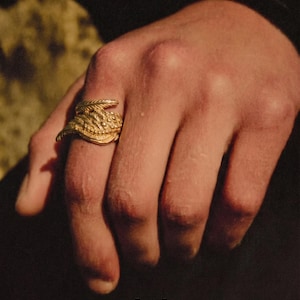 May include: A gold ring with a detailed, textured design is worn on a hand. The ring has a layered appearance. The word "dusk." is printed in white at the bottom of the image.