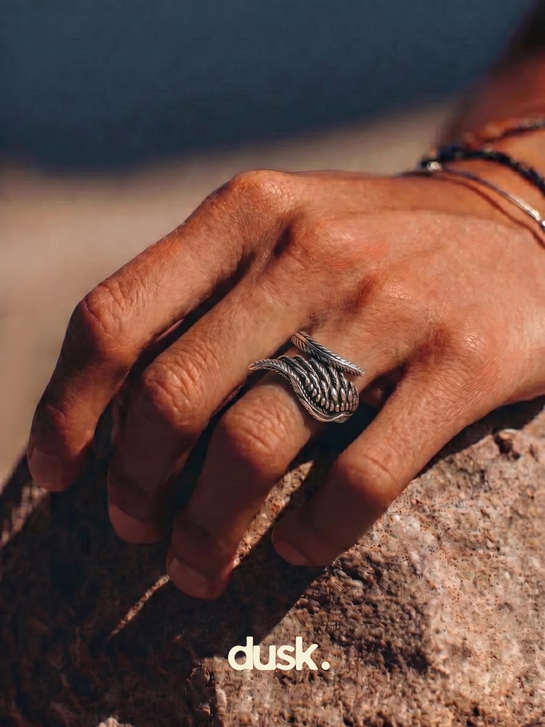 May include: A silver ring with a woven design is worn on a finger. The ring has a textured appearance and is set against a natural background. The word "dusk." is printed in white at the bottom of the image.