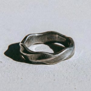 May include: A silver ring with a textured, undulating design. The ring has an organic shape and a matte finish. The word "dusk." is printed in a dark colour at the bottom of the image.