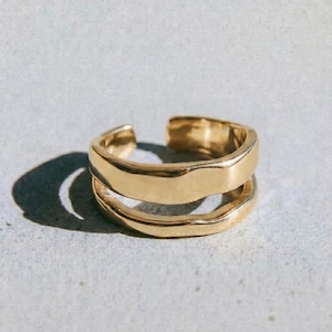 May include: A gold-colored ring with a double-band design. The ring has a smooth, polished finish and a modern, open design. The word "dusk." is printed in black at the bottom of the image.