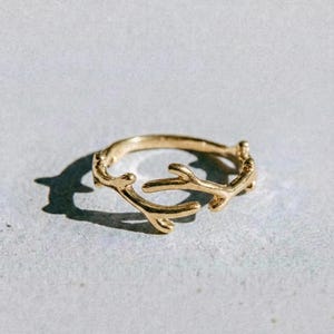 May include: A gold-colored ring with a branch-like design. The ring features multiple small, twig-like projections, creating a natural, organic aesthetic. The word "dusk." is printed in black at the bottom of the image.