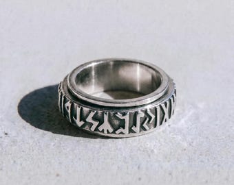 May include: A silver ring with engraved runic symbols. The ring has a rotating band and a polished finish. The word "dusk" is printed in a dark font at the bottom of the image. The ring is displayed on a light gray surface.