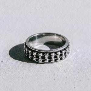 May include: A silver ring with a textured design. The ring has a series of small, connected cylindrical shapes around the band. The word "dusk." is printed in a dark colour at the bottom of the image.