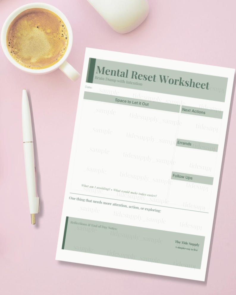 May include: A white worksheet titled "Mental Reset Worksheet" with sections for notes, next actions, and errands. A cup of coffee and a pen are next to the worksheet on a pink surface.