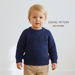 Op de afbeelding: Een marineblauwe gebreide trui met een geribbelde textuur, gedragen door een jong kind. De trui heeft een ronde hals en lange mouwen. De tekst "SEWING PATTERN" en "PDF PATTERN" staat op de afbeelding.