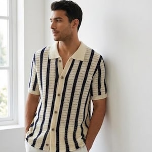 May include: Cream-colored polo shirt with vertical navy blue stripes. The short-sleeved shirt has a button-down front and a collared neckline. The shirt is made of a breathable, open-weave fabric.