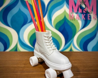 May include: A white roller skate-shaped pencil holder with colorful pencils. The pencil holder is a white boot design with laces and wheels. The background is a retro blue, green, and white pattern. The text "MOODY MOM MAKES" is in pink.