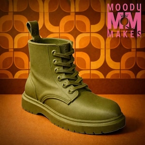 Può includere: Stivale da combattimento verde oliva con allacciatura e linguetta. Lo stivale ha una suola spessa ed è ambientato su uno sfondo a motivi retrò. Il testo "MOODY M&M MAKES" è visibile in alto a destra.