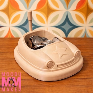 Puede incluir: Un banco de monedas de madera de color claro con forma de coche lleno de monedas. El banco tiene una estrella en la parte delantera y un asa de madera. El banco está sobre una superficie de madera.