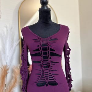 Op de afbeelding: Een pruimkleurige bodysuit met lange mouwen en een V-hals. De voorkant en de mouwen hebben een uitgesneden ontwerp. De bodysuit wordt getoond op een zwarte mannequin.