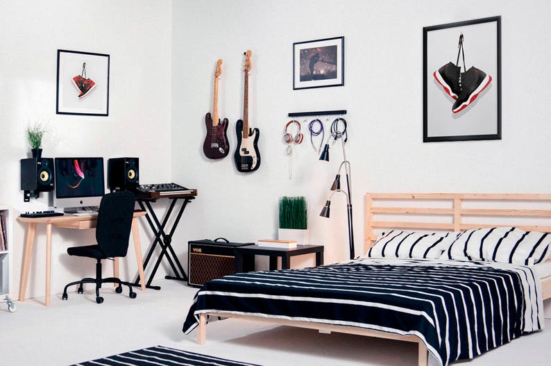 K&ouml;nnte beinhalten: Ein Schlafzimmer mit einem Bett, einem Schreibtisch und einer Gitarre, die an der Wand h&auml;ngt. Das Bett hat eine schwarz-wei&szlig; gestreifte Bettdecke. Der Schreibtisch hat einen Computer, eine Tastatur und zwei Lautsprecher. Die Gitarre ist schwarz und hat ein wei&szlig;es Schlagbrett. An der Wand h&auml;ngt ein gerahmtes Bild von einem Paar rot-schwarzer Turnschuhe.