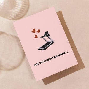 Puede incluir: Tarjeta de felicitación rosa con una ilustración de cinta de correr y tres corazones rojos. El texto en la tarjeta dice: "YOU'RE LIKE A TREADMILL..." La tarjeta está sobre un sobre marrón.