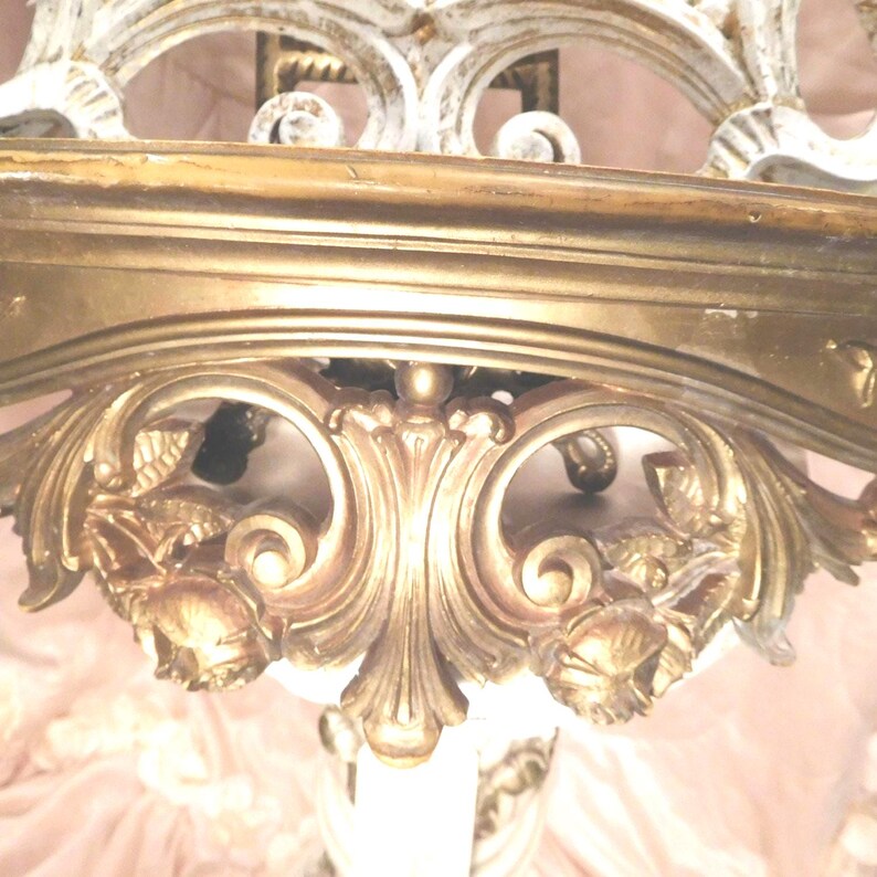 Puede incluir: Un estante de pared con acabado en tono dorado, que presenta intrincados tallados de volutas y motivos florales. El estante tiene una superficie superior horizontal lisa y un soporte decorativo ornamentado debajo con relieves detallados.