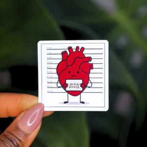 Peut inclure: Un autocollant carr&eacute; repr&eacute;sentant un c&oelig;ur de dessin anim&eacute; dans un alignement policier. Le c&oelig;ur rouge tient une pancarte avec l'inscription "arr&ecirc;t cardiaque". L'arri&egrave;re-plan est vert flou.