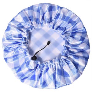 May include: A round, blue and white gingham patterned shower cap with a shiny, satin-like finish. The cap features a gathered, elasticized edge and a black adjustable drawstring cord with a small plastic toggle for securing the fit.