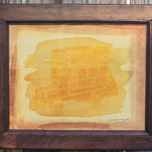 May include: A framed watercolor painting of a vintage double-decker bus in shades of yellow and orange. The artwork is set against a light background and framed in a dark brown wooden frame. The artist's signature is visible.