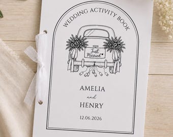 May include: A white wedding activity book with a black line drawing of a car decorated with flowers and a Just Married sign. The text reads Wedding Activity Book, Amelia and Henry, and 12.06.2026. The booklet is bound on the left side with a white ribbon.