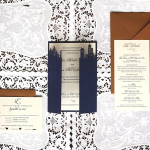 Puede incluir: Un conjunto de invitaciones de boda con un esquema de color azul marino y dorado. Las invitaciones presentan un dise&ntilde;o de ciudad y el texto "Con gran alegr&iacute;a les solicitamos el placer de su compa&ntilde;&iacute;a en la boda de..." y "Los detalles".