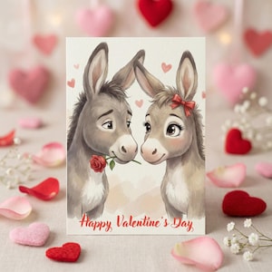 Puede incluir: Tarjeta de San Valentín con una ilustración de dos burros. Uno sostiene una rosa roja, frente al otro con un lazo rojo. La tarjeta tiene el texto "Happy Valentine's Day" en rojo, con corazones rosas en el fondo.