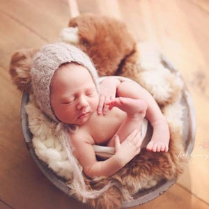 May include: A newborn baby wearing a knitted hat sleeps peacefully in a basket lined with faux fur. The baby is curled up with its legs tucked in and its arms wrapped around itself.