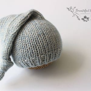 Puede incluir: Un gorro de bebé de punto azul claro con una cola larga y puntiaguda. El gorro está hecho de un hilo suave y texturizado y tiene un diseño simple y clásico.