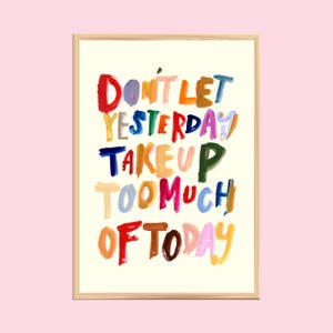 Puede incluir: Una impresión artística enmarcada con el texto "Don't let yesterday take up too much of today" en letras coloridas y de estilo manuscrito. Las palabras son de varios colores, incluyendo rojo, azul, amarillo y verde, sobre un fondo crema.