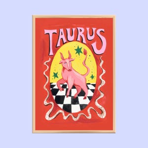 May include: A framed art print featuring the word "TAURUS" in pink above a pink bull illustration. The bull stands on a black and white checkered floor within a yellow oval, set against a red background with green stars and white wavy lines.