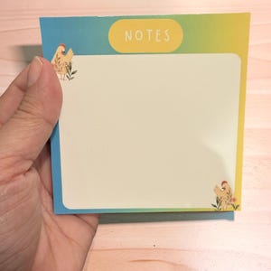 May include: A rectangular notepad with a gradient blue, green, and yellow border. The notepad has a white interior with the word "NOTES" in a yellow oval. Chicken illustrations are in the corners.