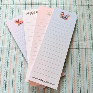 May include: Four vertical rectangular notepads with lined paper. The first features a hummingbird, the second a row of birds, the third a floral sprig, and the fourth a butterfly illustration. Each notepad has a distinct pastel background color.