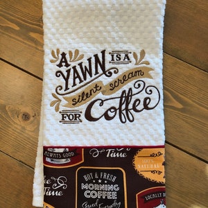 May include: White kitchen towel with the embroidered text "A Yawn is a silent scream for Coffee". The towel has a red and brown border with a coffee themed pattern.
