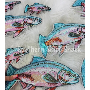 May include: Multiple fish-shaped patches decorated with iridescent sequins in shades of pink, blue, and silver. Each patch features a detailed fish design with a prominent eye, fins, and a scaled body texture created by the layered sequin application.
