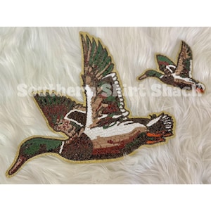 May include: Two beaded duck patches in flight. The ducks feature brown, green, and white details with gold outlines. The text "Southern Shirt Shack" is partially visible.