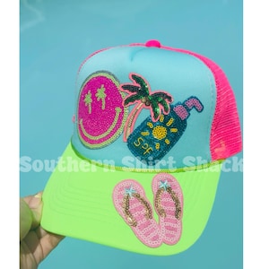 Op de afbeelding: Een neon groene en blauwe truckerpet met een roze mesh achterkant. De pet heeft pailletten ontwerpen van een smiley, palmboom, zonnebrandcr&egrave;me fles en slippers. De tekst "Southern Shirt Shack" is op de klep gedrukt.