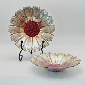 May include: Two decorative glass plates shaped like flowers. The plates have a silver and gold iridescent finish with a red center. One plate is on a black metal stand, and the other is a smaller bowl.
