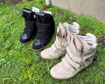 Könnte beinhalten: Zwei Paar Keil-Sneaker auf grünem Gras. Ein Paar ist schwarz mit drei Klettverschlüssen, das andere ist beige mit drei Klettverschlüssen. Beide Paare haben ein High-Top-Design.