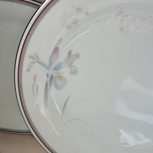 May include: White ceramic dinner plates with a floral design. The plates have a gray and burgundy border. The floral design features light blue, pink, and green flowers and leaves.