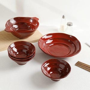 May include: A collection of glossy, deep red ceramic bowls. The set includes various sizes, from small individual bowls to a large serving bowl with a handle. The bowls have a rustic, handcrafted appearance, suitable for serving soups, salads, or other dishes.