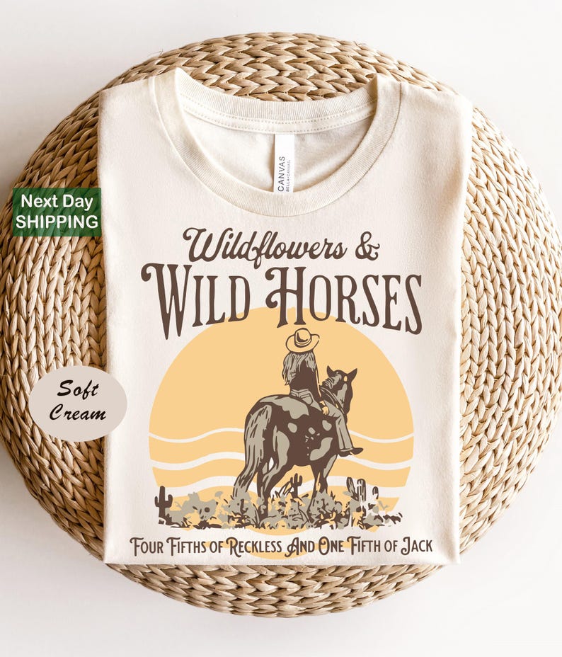 A white t-shirt with a graphic design depicting a cowboy riding a horse, with the text "Wildflowers & Wild Horses" and "Four Fifths of Reckless and One Fifth of Jack" printed on it.