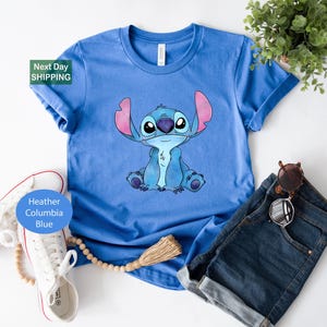 a blue t-shirt with a cartoon character printed on it, along with a pair of jeans, sunglasses, and a plant.
