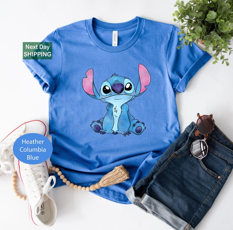 a blue t-shirt with a cartoon character printed on it, along with a pair of jeans, sunglasses, and a plant.