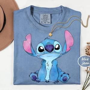 A blue t-shirt with a cartoon character printed on it, along with a necklace and a hat.