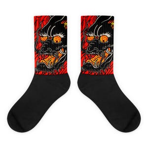 May include: Pair of black socks featuring a detailed dragon design. The dragon is black with orange and yellow accents, set against a red background. The socks are a crew length, suitable for various occasions.