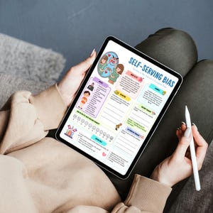 May include: A digital tablet displaying a colorful infographic titled "Self-Serving Bias." The graphic includes illustrations, text, and a diagram. A white stylus is held in the hand. The tablet is held on a person's lap.