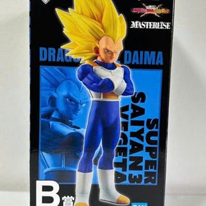 Puede incluir: Figura de acción en caja de Super Saiyan 3 Vegeta de Dragon Ball Daima. La figura tiene pelo amarillo puntiagudo, un atuendo azul y blanco, y está en una pose dinámica. La caja presenta el logotipo de Dragon Ball Daima y texto japonés.