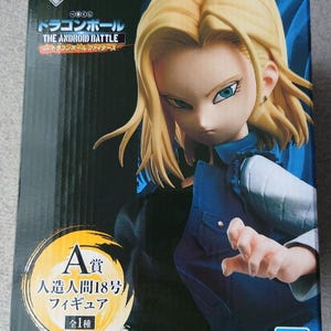 May include: A rectangular product box featuring a Dragon Ball Super Android 18 figure. The box displays the character with blonde hair, a blue vest, and a black shirt. Text includes Dragon Ball The Android Battle, A-prize, and Bandai logo.
