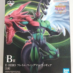 May include: A box featuring a colorful action figure of E-Hero Flame Wingman. The figure is a combination of red, green, and black, with a dragon-like head on one side. The box includes Japanese text and the Bandai Namco logo.